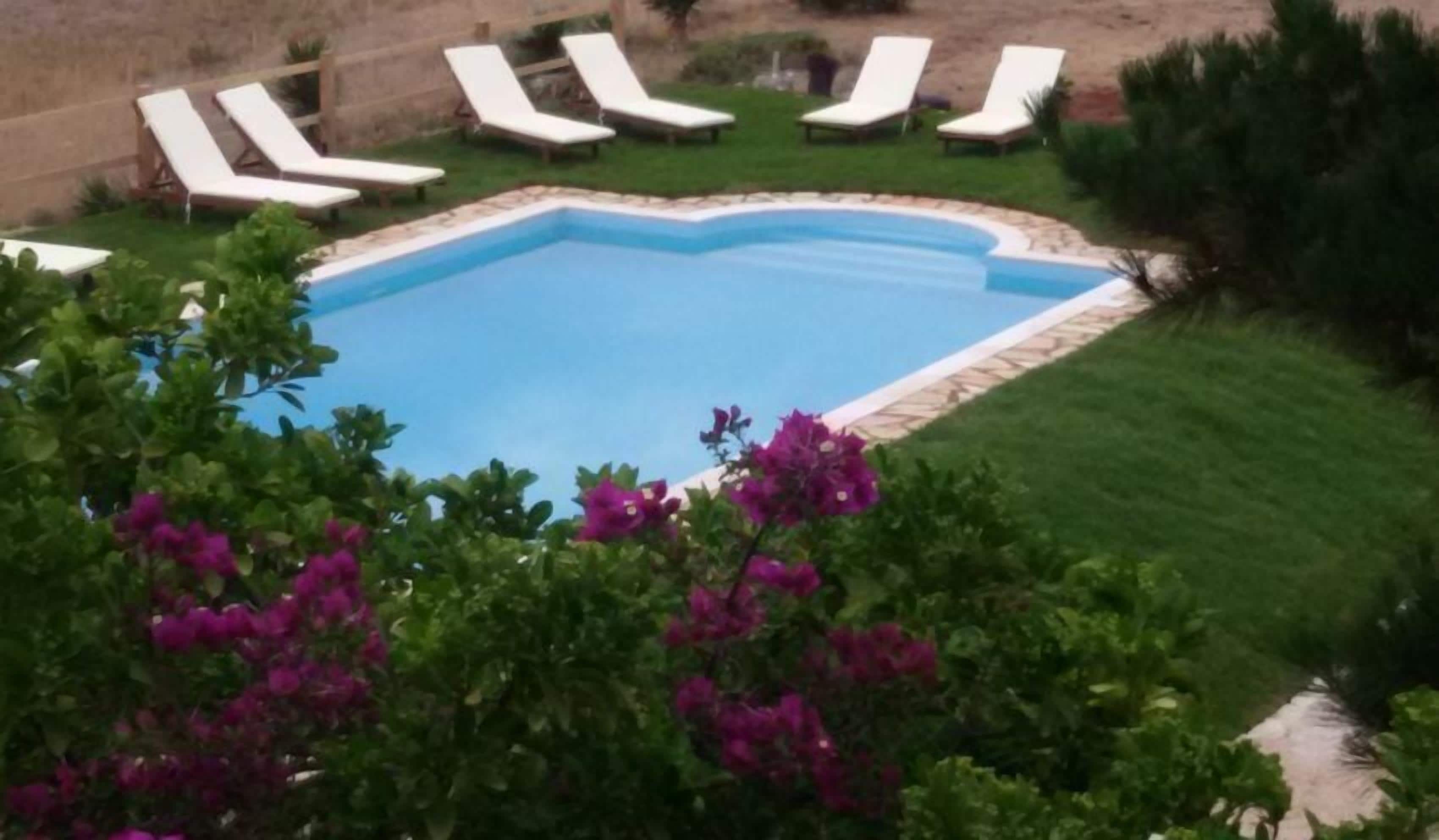 Una piscina rodeada de sillas reclinables blancas y flores moradas.