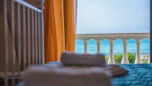Una cama con vista al océano a través de una ventana con balaustrada blanca.