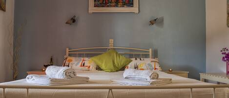 A neatly made bed with multiple towels, a green pillow, and a painting above it.