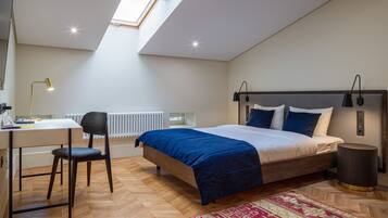A bedroom with a bed, desk, chair, radiator, and a skylight.