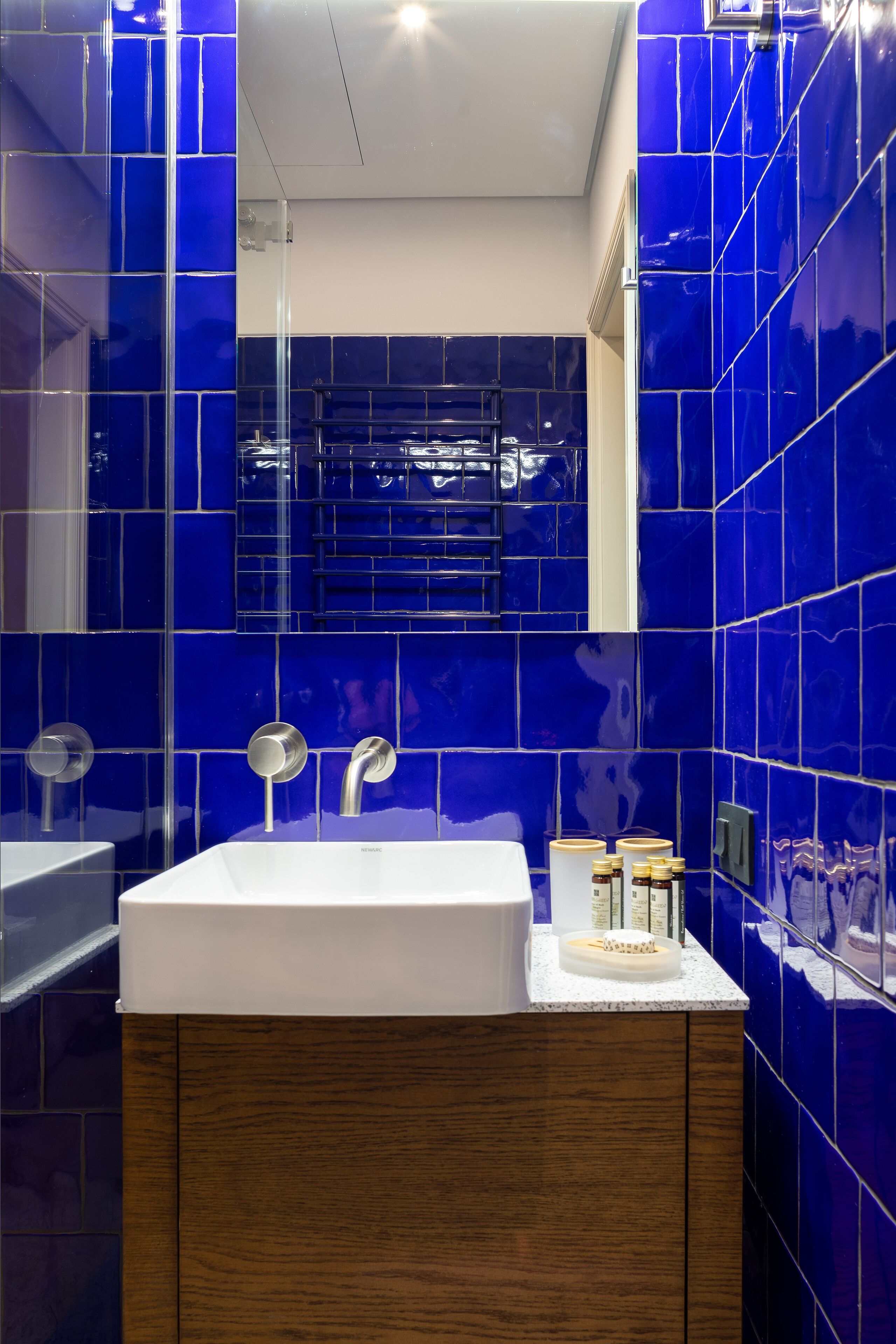 A modern bathroom with a white sink, wooden cabinet, and blue-tiled walls.