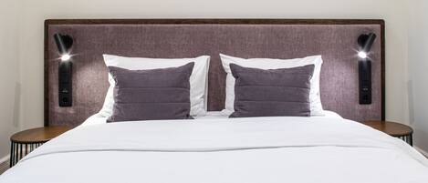 A neatly made bed with a white duvet and two dark pillows, flanked by two bedside tables with lamps.