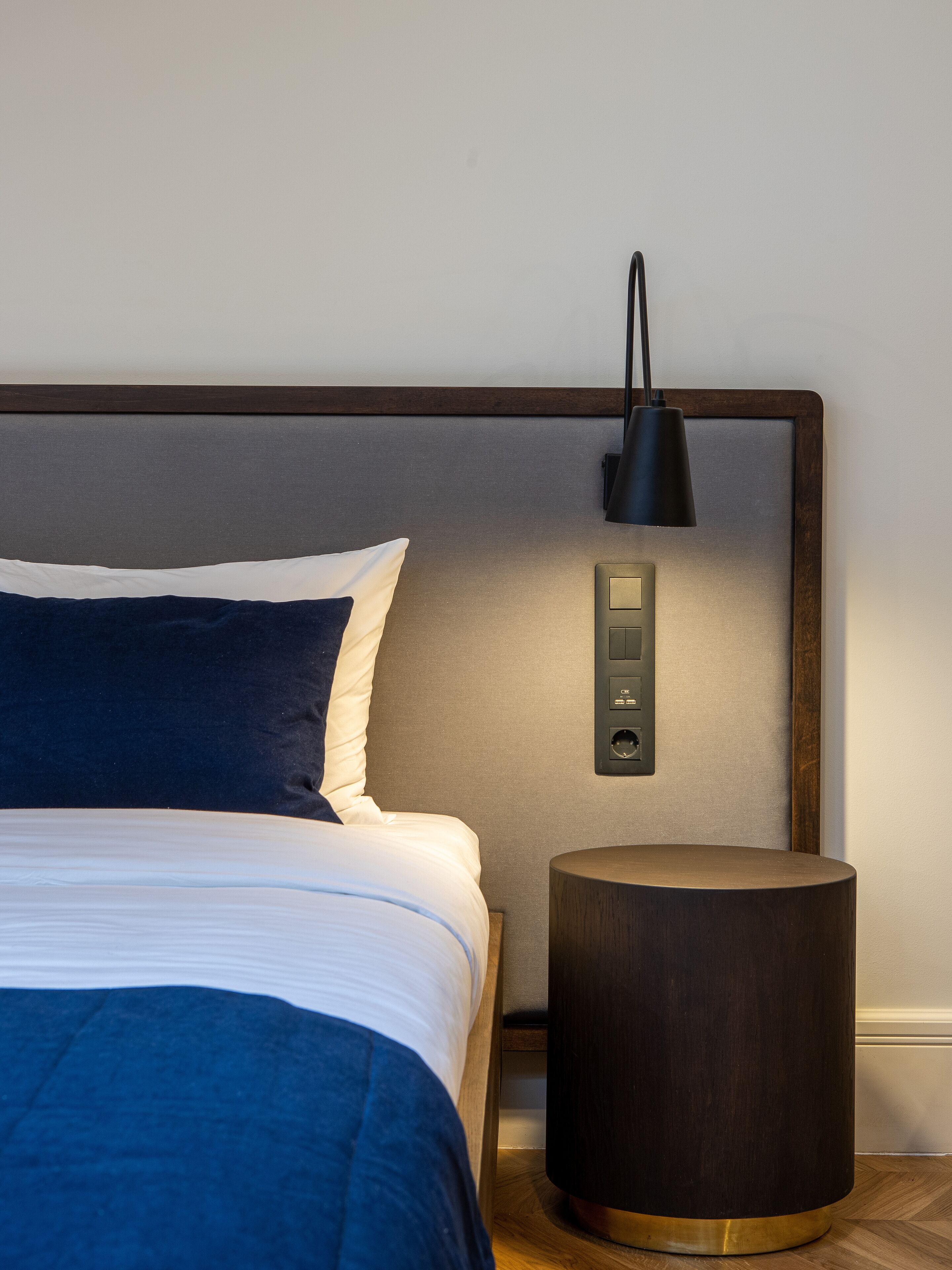 Ein ordentlich bezogenes Bett mit Kopfteil, einer Nachttischlampe und einem Holznachttisch.