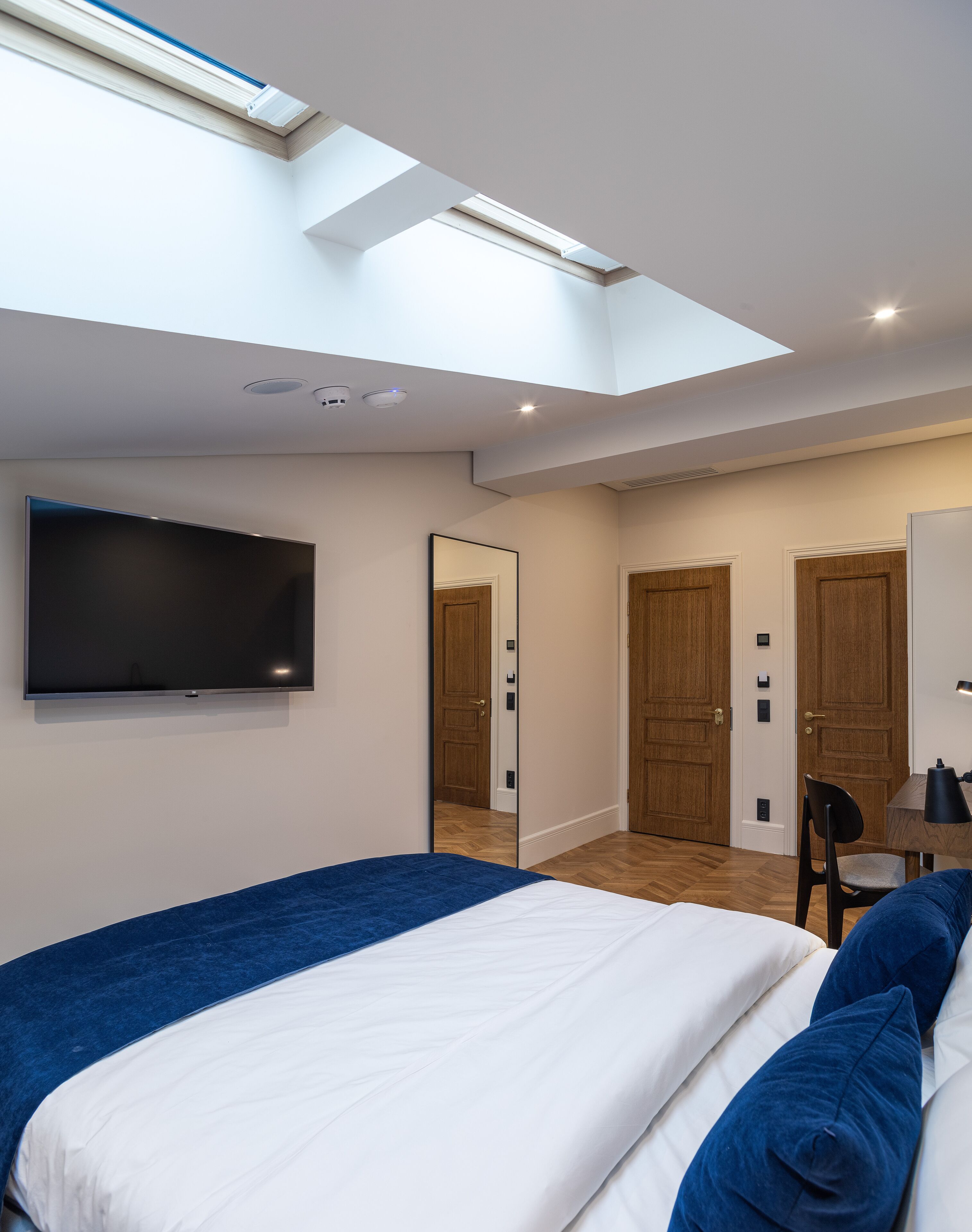 Un dormitorio moderno con una cama grande, un televisor de pantalla plana, un tragaluz y una puerta de madera.