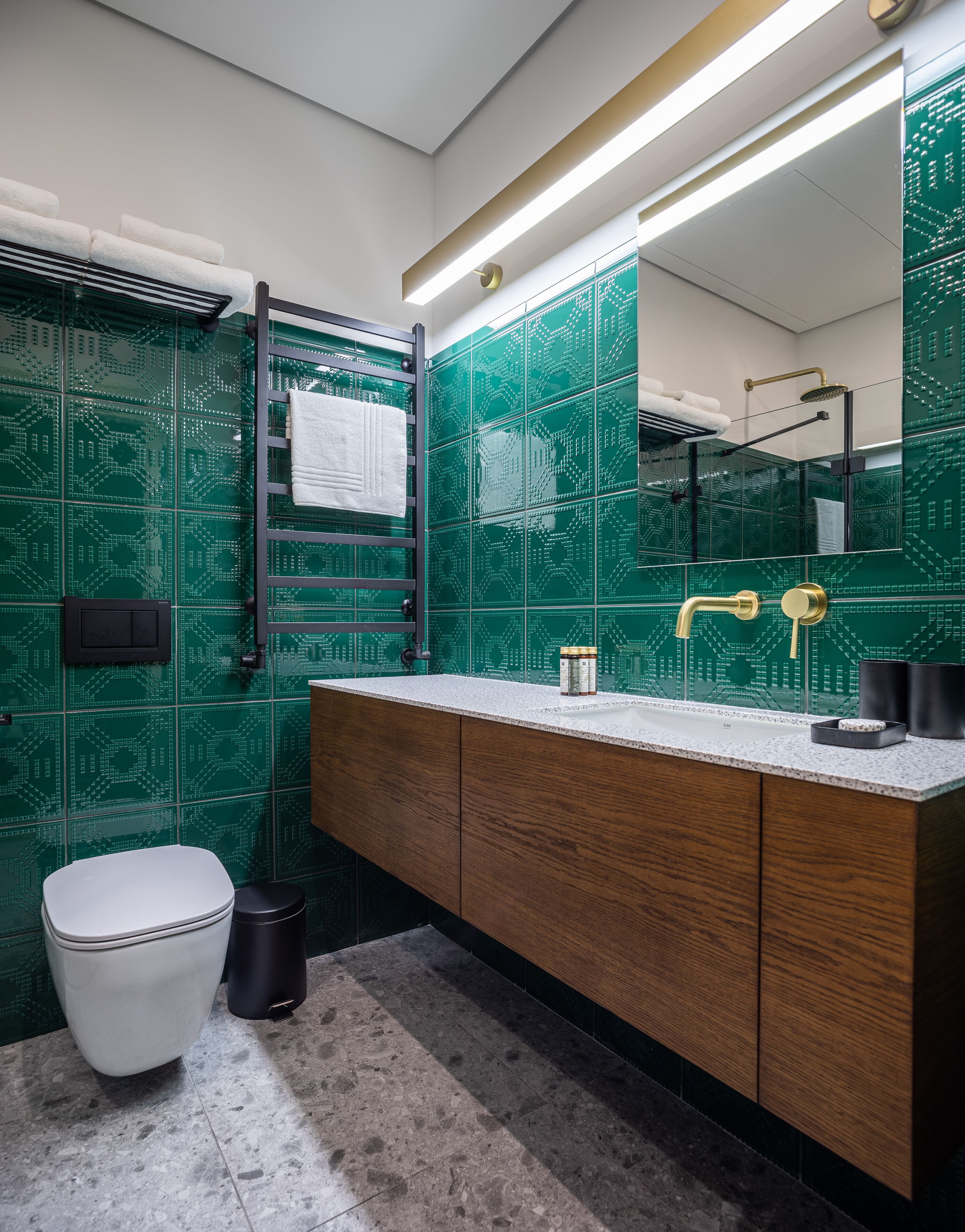 A modern bathroom with green patterned tiles, a white toilet, a wooden vanity, and a large mirror.