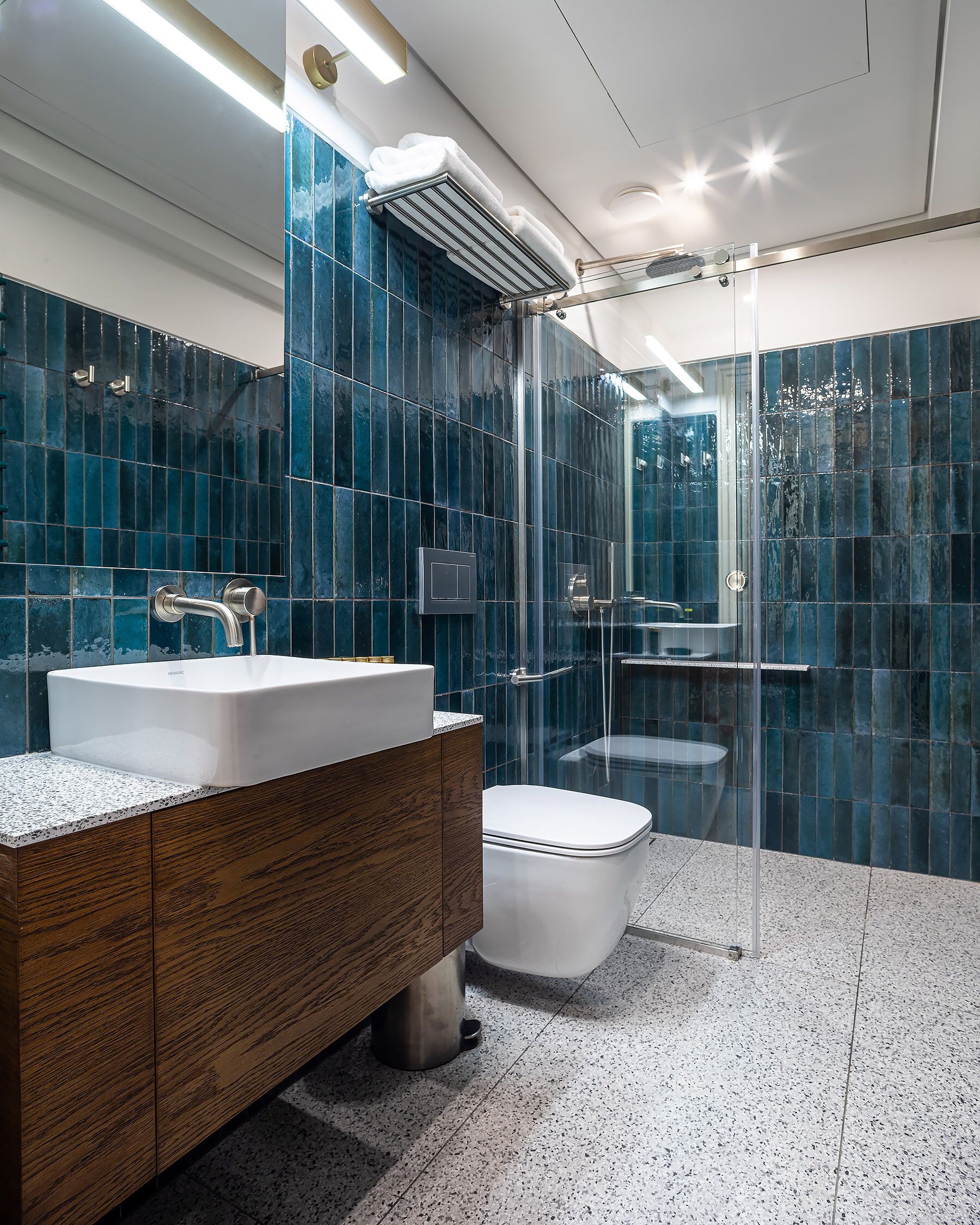 Un baño moderno con cabina de ducha de vidrio, lavamanos blanco y tocador de madera.