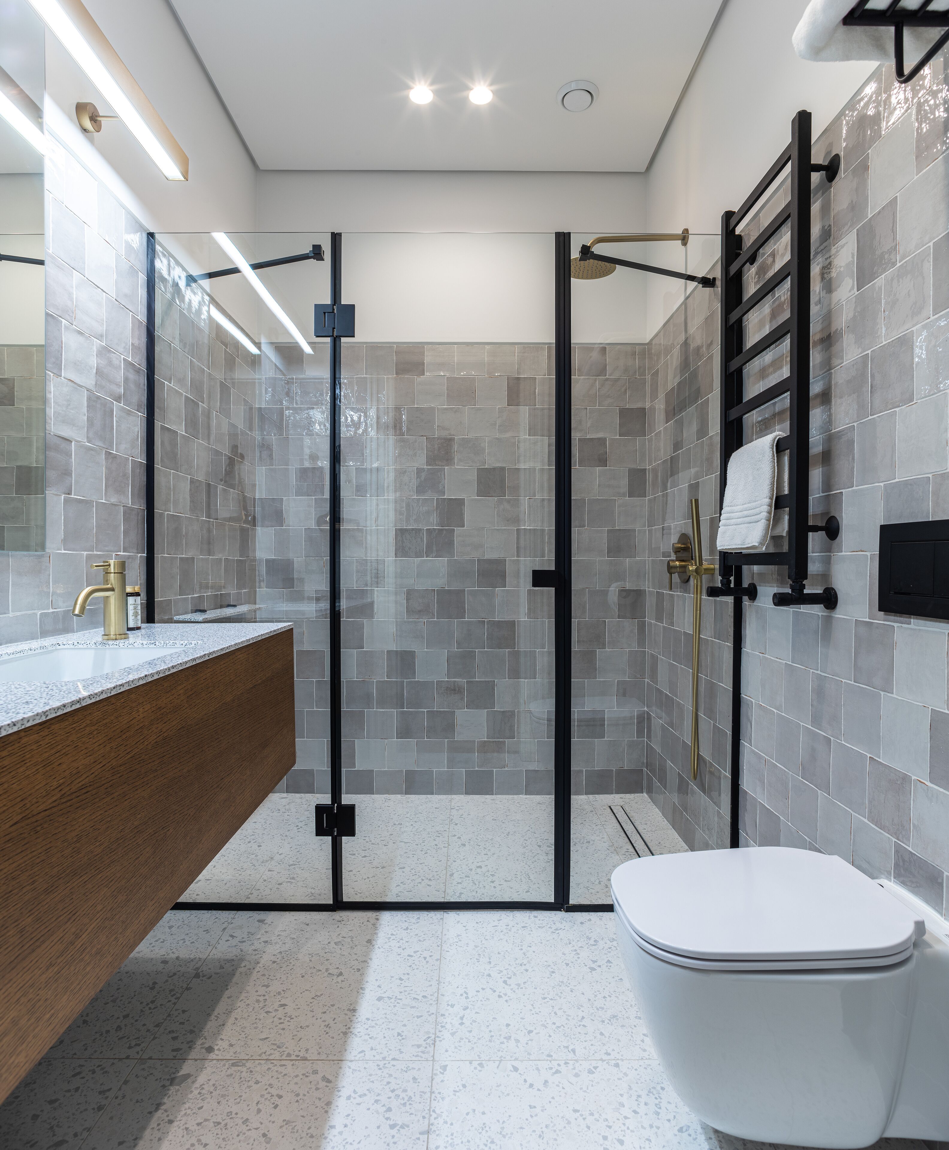 A modern bathroom with a glass-enclosed shower, a wooden vanity, and a white toilet.