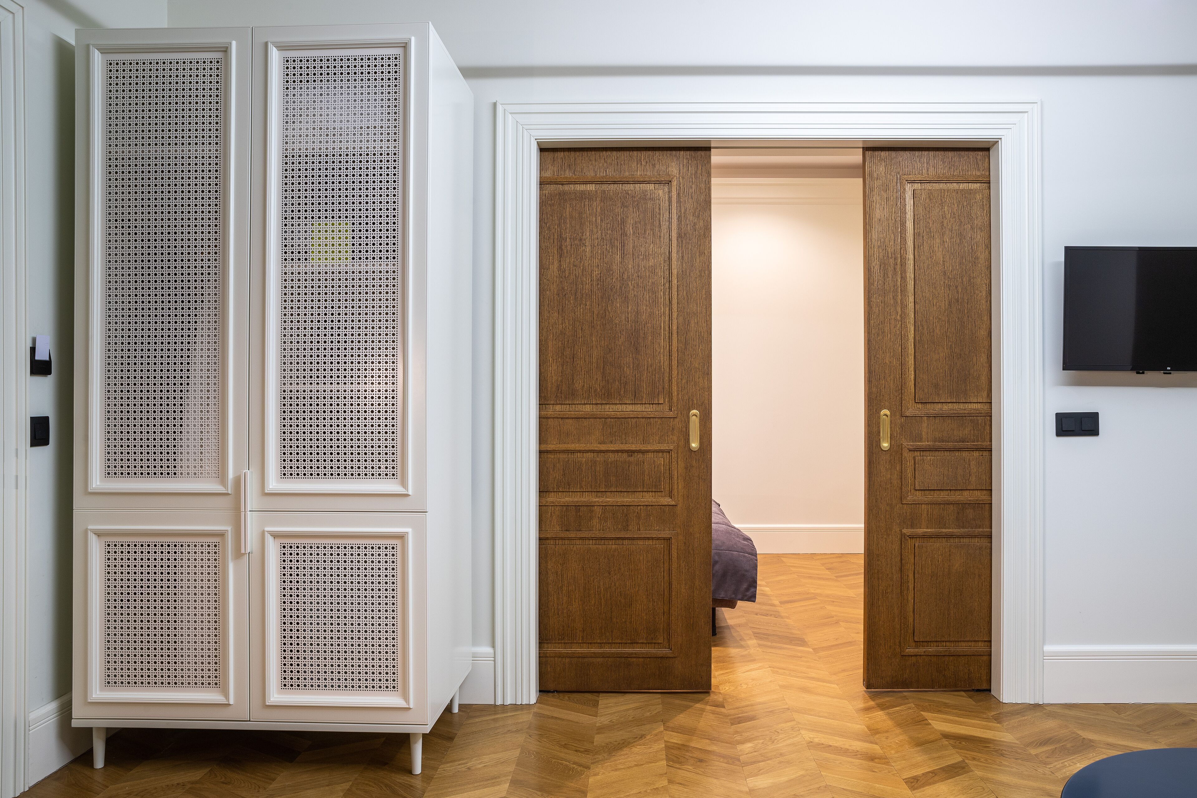 Ein Zimmer mit einem Holfischschrank, einem Bett und einem Fernseher an der Wand.