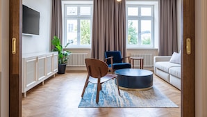 A modern living room with a sofa, two chairs, a coffee table, a TV, and large windows with curtains. - On The Square  (Lviv)