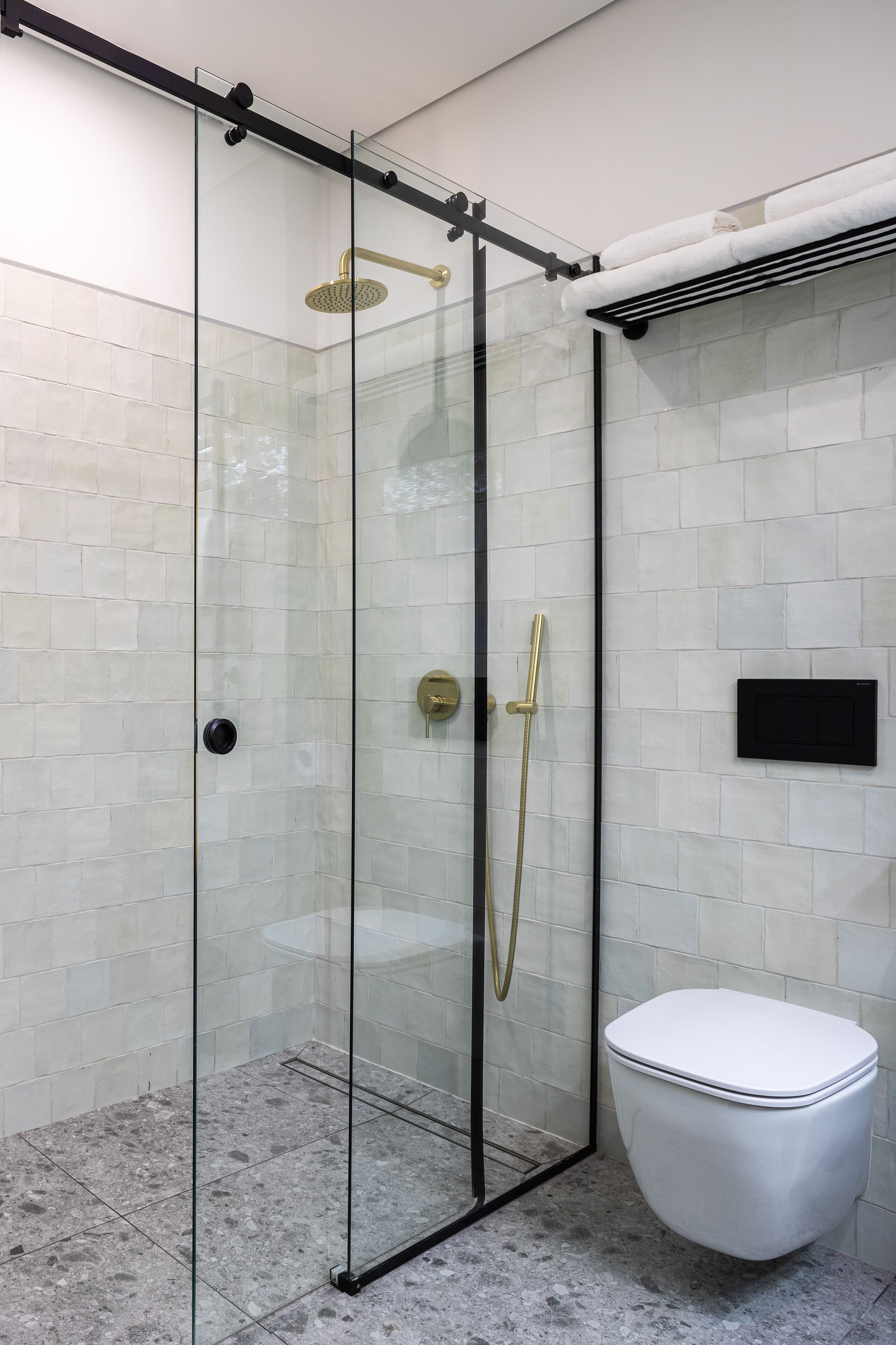 Cabina doccia in vetro con soffione dorato e WC bianco.