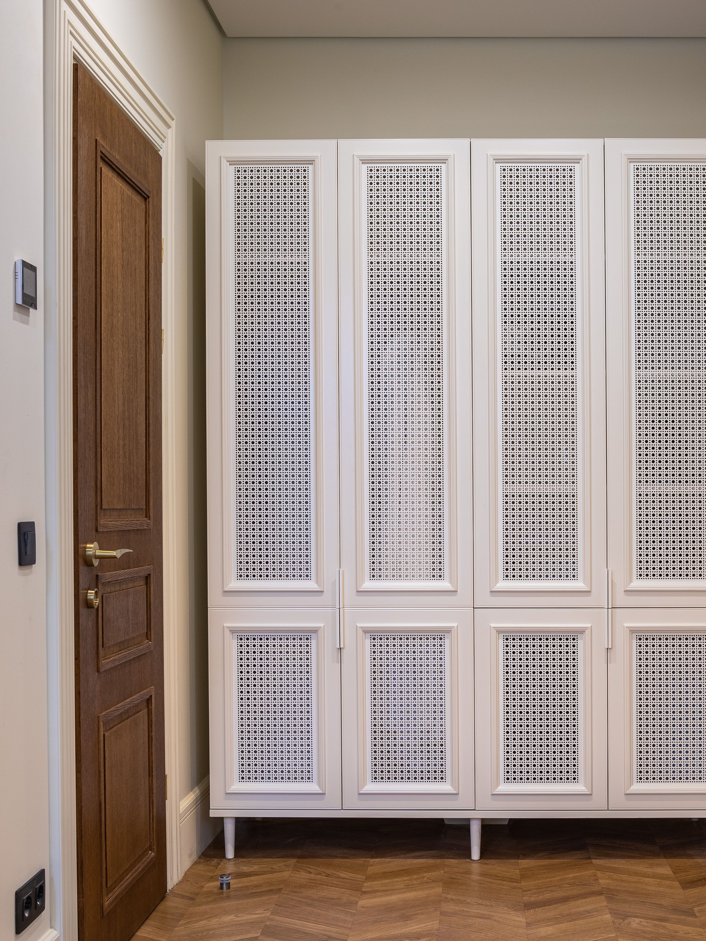 Une pièce dotée d’une porte en bois, de meubles blancs aux panneaux perforés et d’un parquet en bois disposé en motif chevrons.