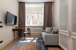 A modern living room with a sofa, a TV mounted on the wall, a desk with a chair, and a large window with curtains. - On The Square  (Lviv)