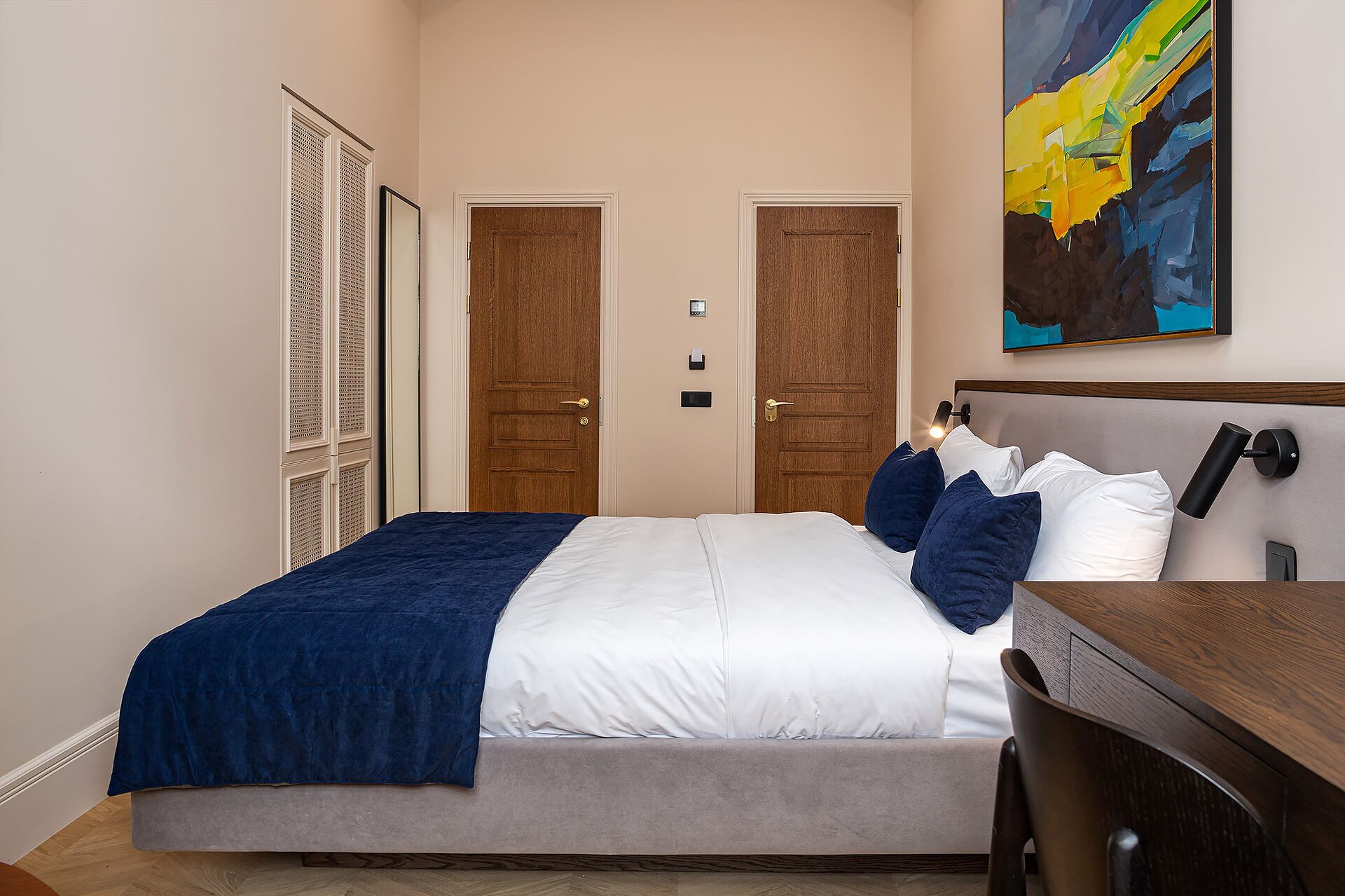 Una habitación de hotel con cama, mesita de noche y escritorio. Hay dos puertas y una ventana.