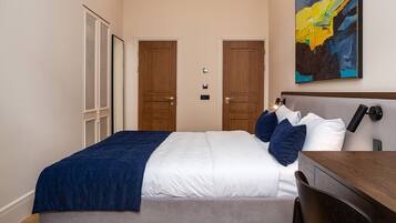 Una habitación de hotel con cama, mesita de noche y escritorio. Hay dos puertas y una ventana.