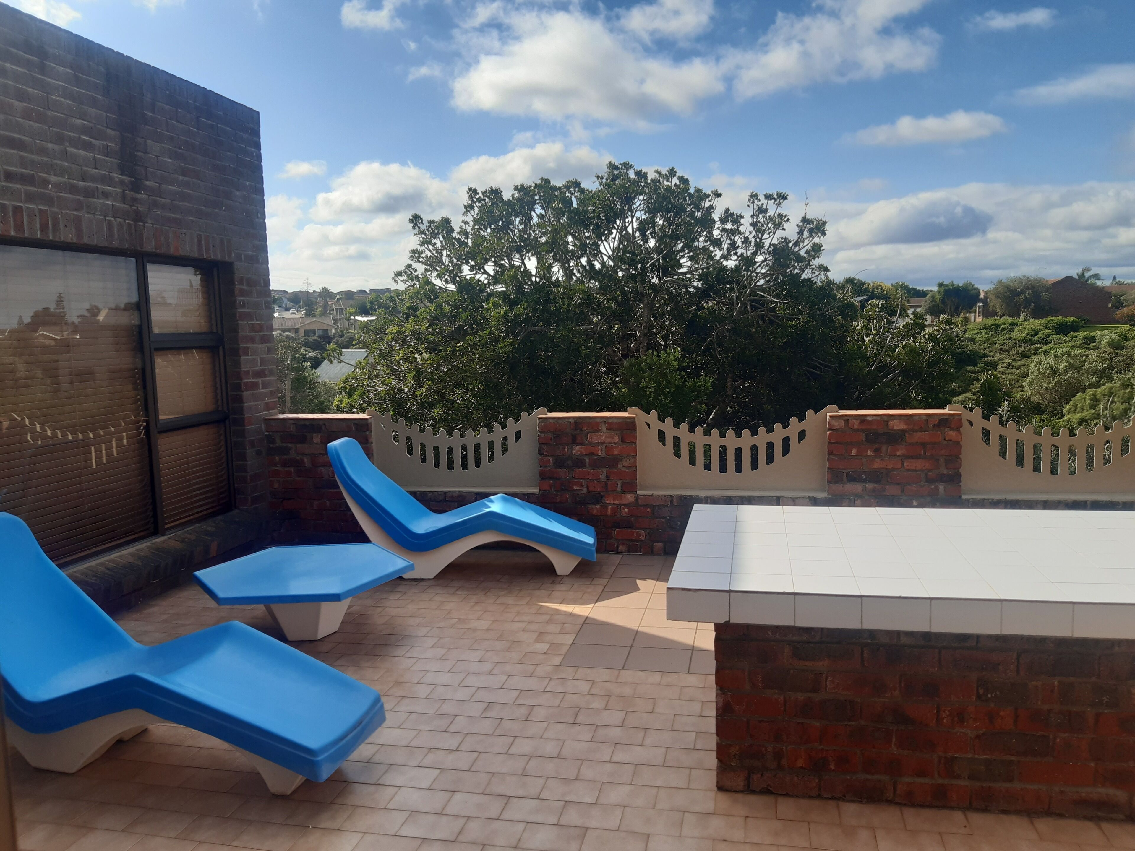 A rooftop terrace with blue lounge chairs, a white table, and a brick wall.
