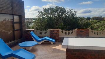 A rooftop terrace with blue lounge chairs, a white table, and a brick wall.