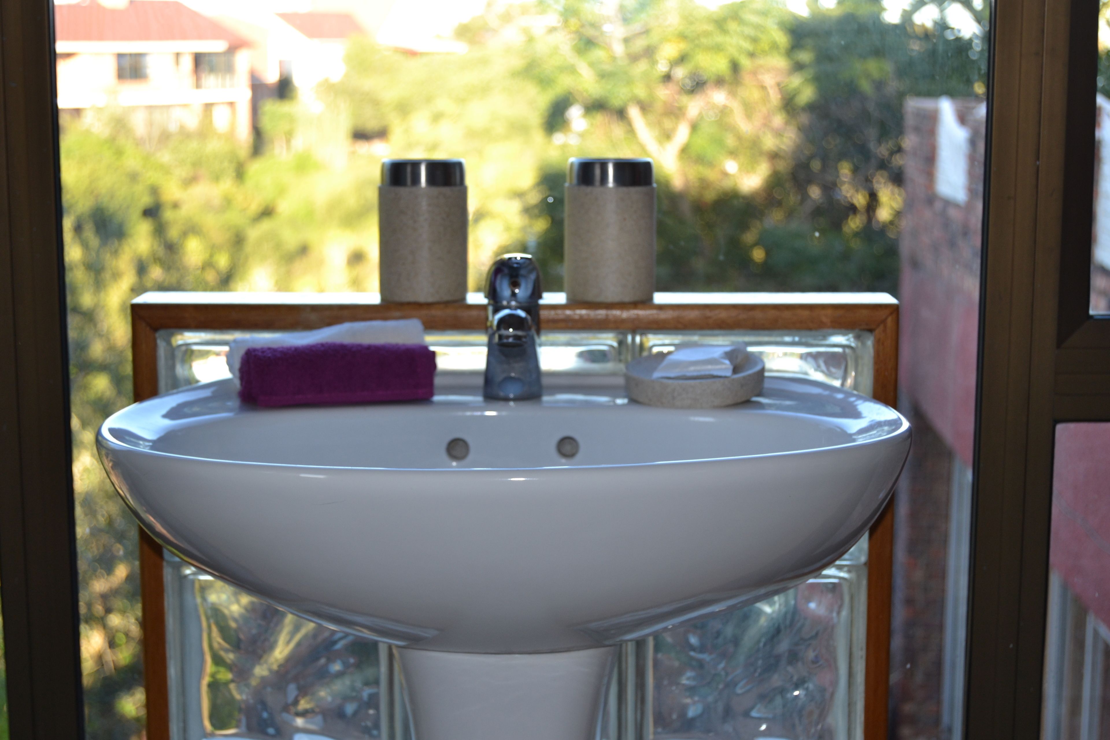 A bathroom sink with a window view, a purple towel, and two cylindrical containers.