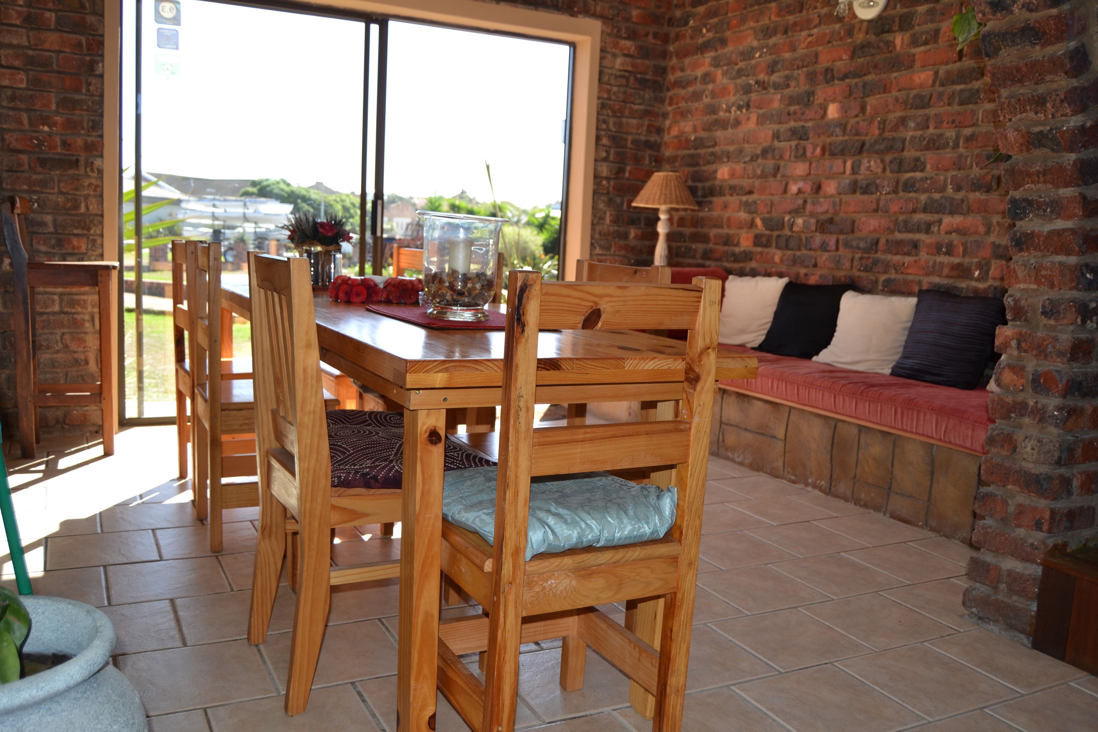 A dining area with a wooden table and chairs, a bench with cushions, and a view through a large window.