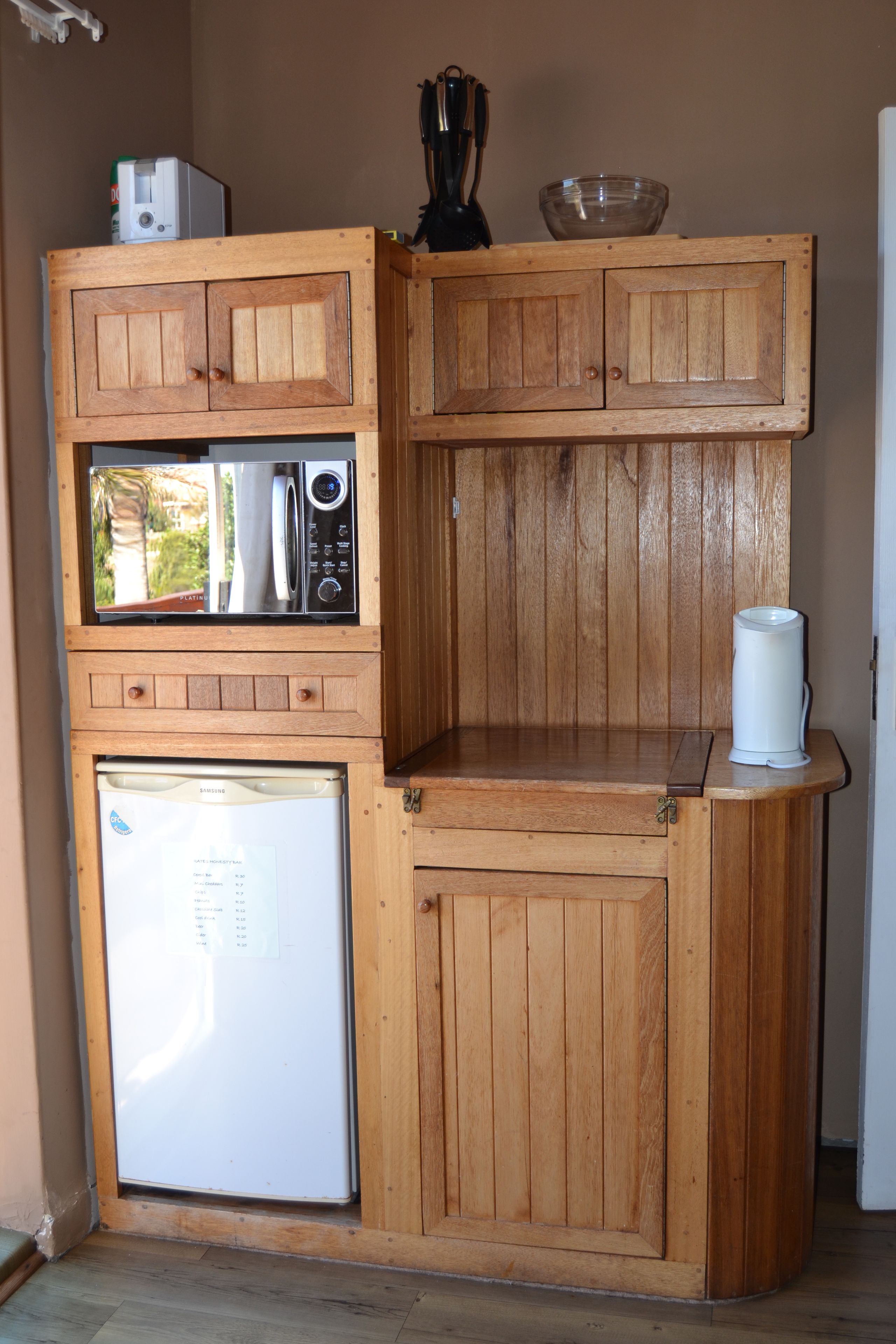 A compact kitchen with wooden cabinetry, a microwave, a refrigerator, and a coffee maker.