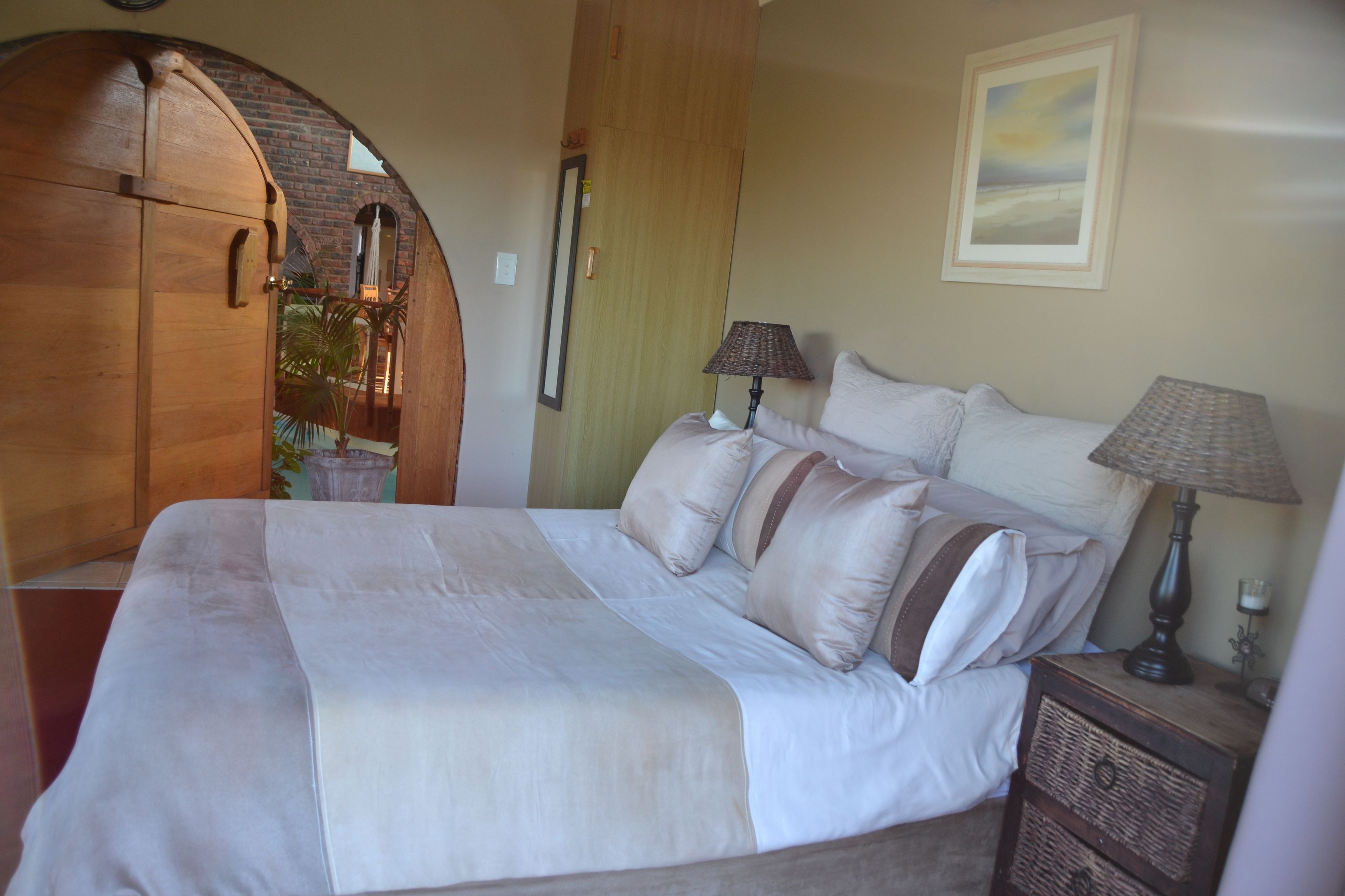 A bedroom with a large bed, two bedside tables with lamps, a wooden wardrobe, and a mirror.