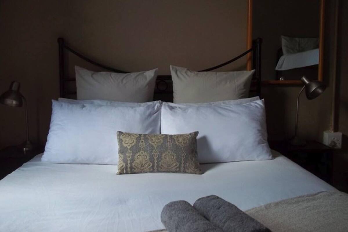 A neatly made bed with white linens and a patterned pillow, two bedside lamps, and a mirror on the wall.