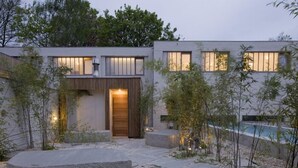 A modern house with a stone patio, a wooden door, and a swimming pool in the background. - Wu Wei (Kortrijk)