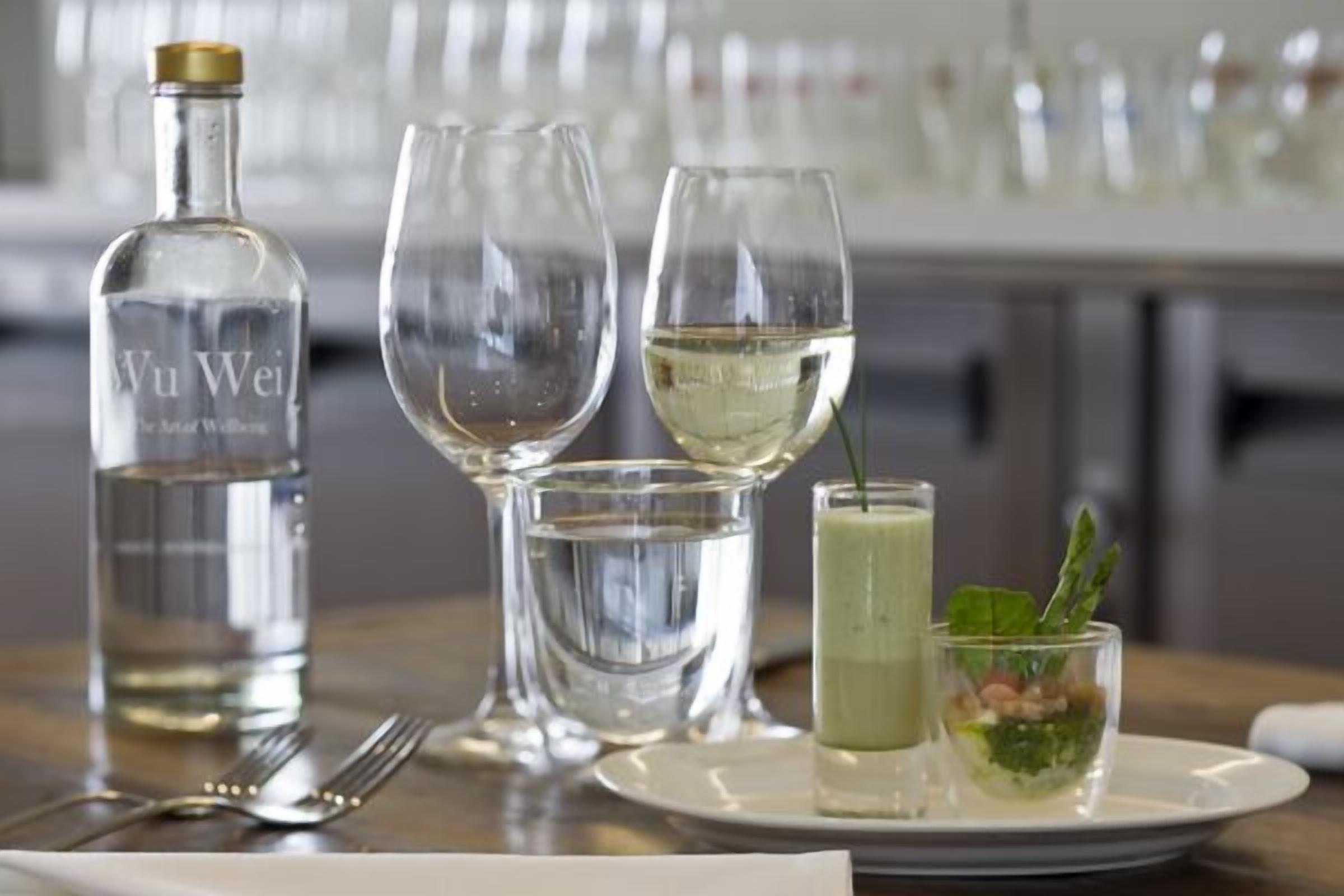 A dining table with a bottle of white wine, two wine glasses, a water glass, and a small dish with a green sauce and herbs.