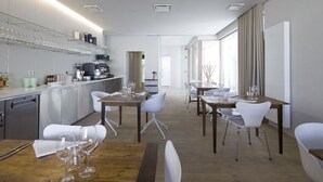 A modern hotel dining area with a long counter, white chairs, and tables set for dining. - Wu Wei (Kortrijk)