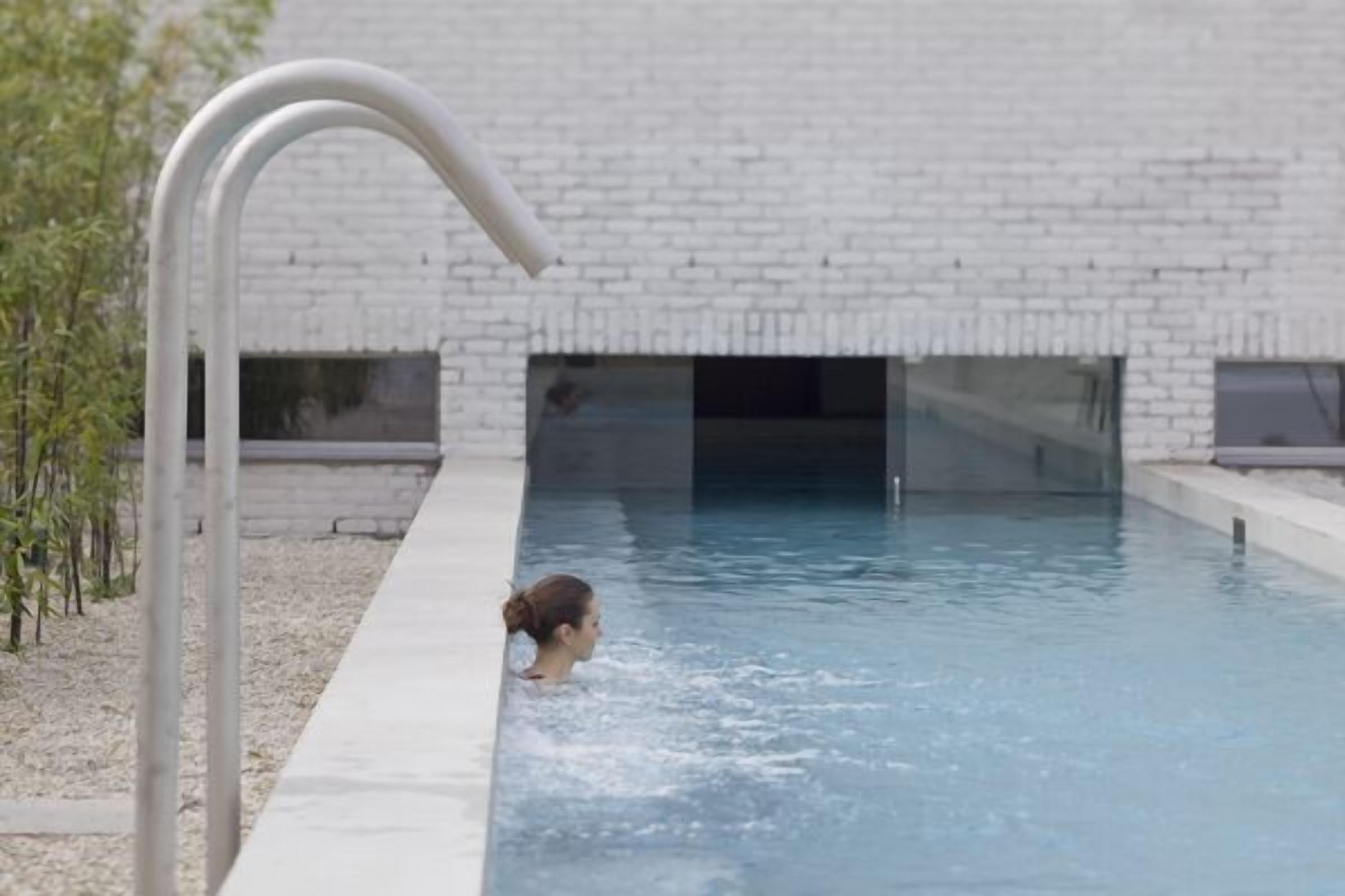 Una piscina con vista despejada al área de la piscina, una barandilla metálica y un edificio de ladrillo blanco al fondo.