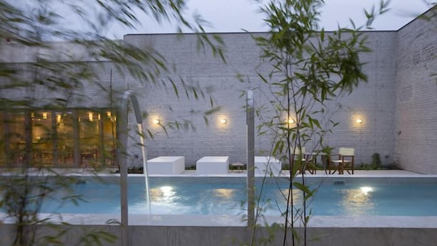 A modern outdoor pool area with a brick wall, seating, and a glass building in the background. - Wu Wei (Kortrijk)