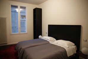 A bedroom with two beds, a radiator, a window, and a black wardrobe. - Bed & Breakfast Parigi (Bologna)