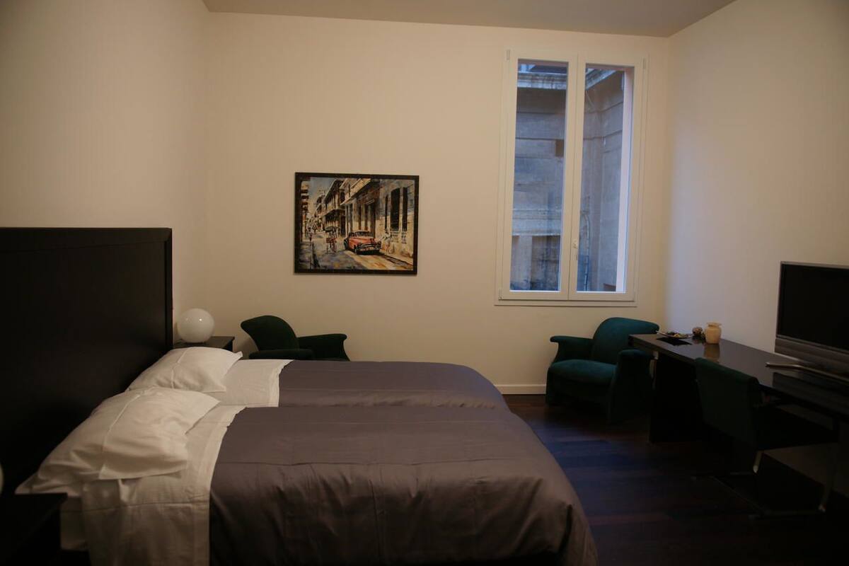 Ein Hotelzimmer mit Bett, Schreibtisch, Stuhl, einem Gemälde und einem Fenster.