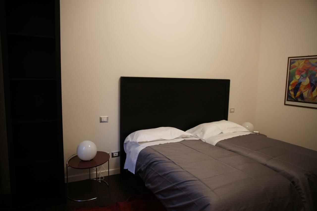 A modern hotel room with a large bed, a small round table with a white spherical object, and a colorful abstract painting on the wall.