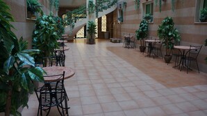 A spacious indoor area with multiple tables and chairs, surrounded by potted plants and a staircase.