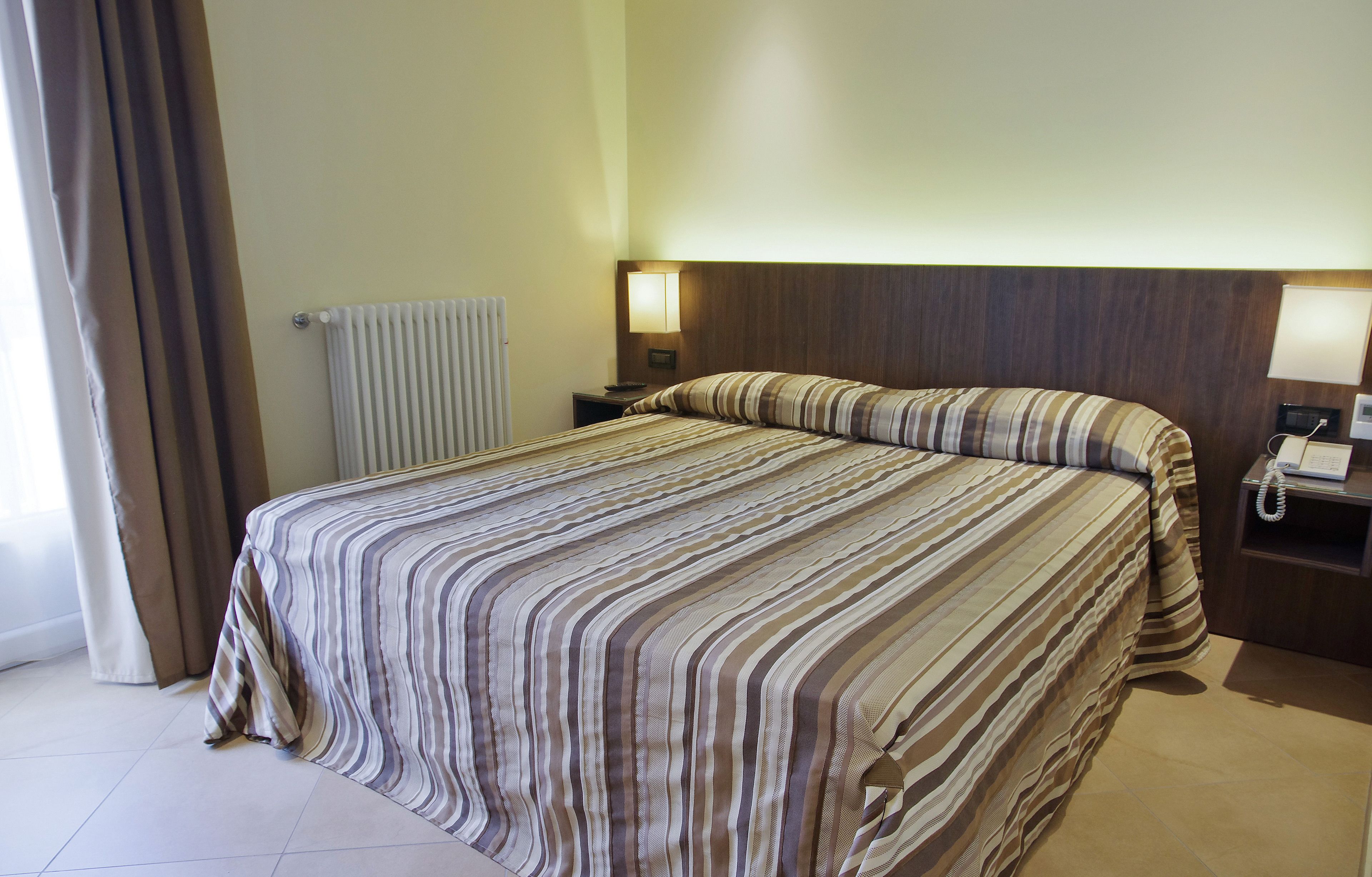 Una habitación de hotel con una cama grande, una mesita de noche con lámpara, teléfono y radiador.