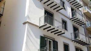 Un edificio de varios pisos con escaleras exteriores, balcones y un cuadro de alarmas contra incendios.