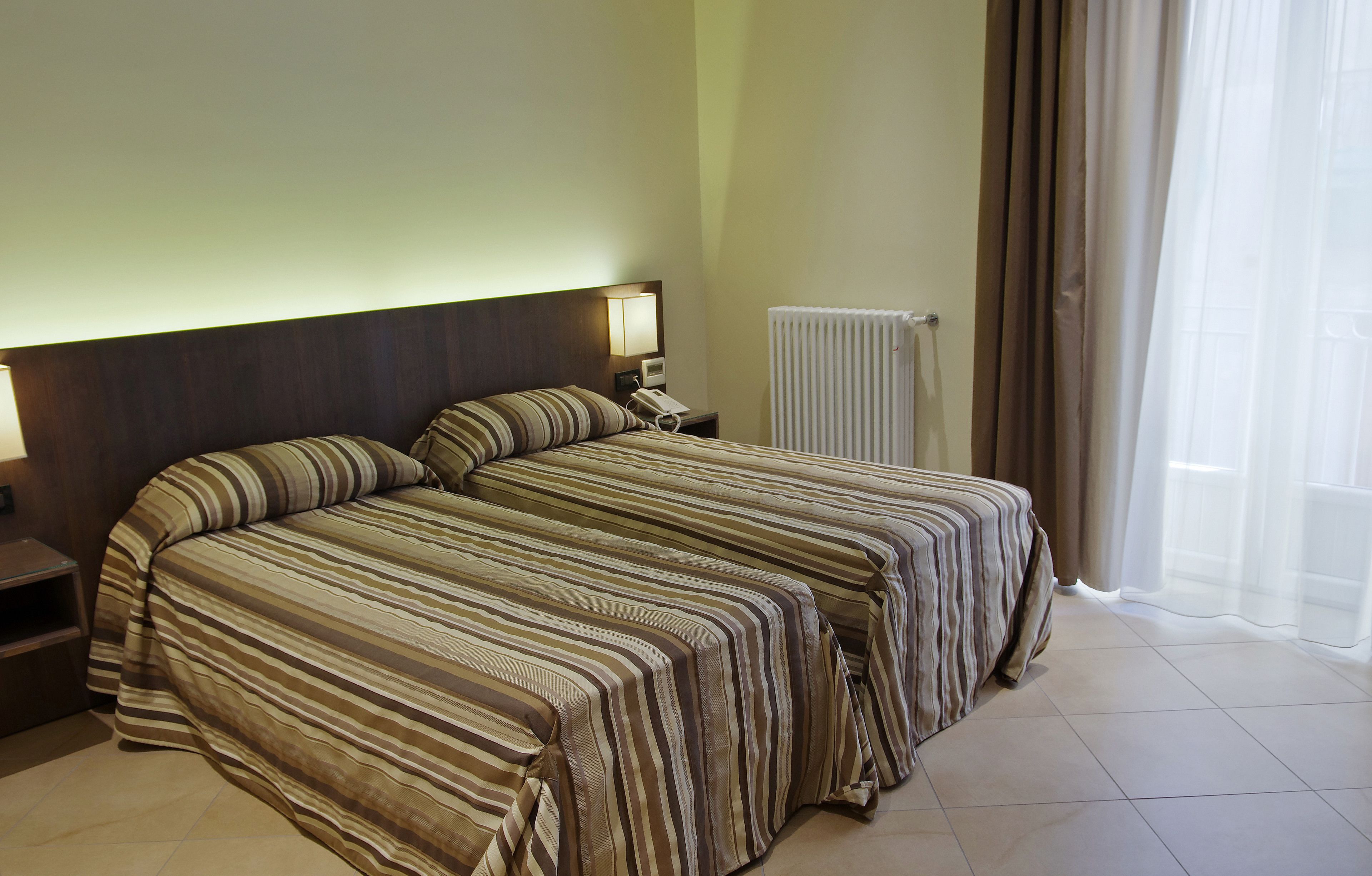 A hotel room with two beds, a nightstand, a lamp, a telephone, and a window with curtains.