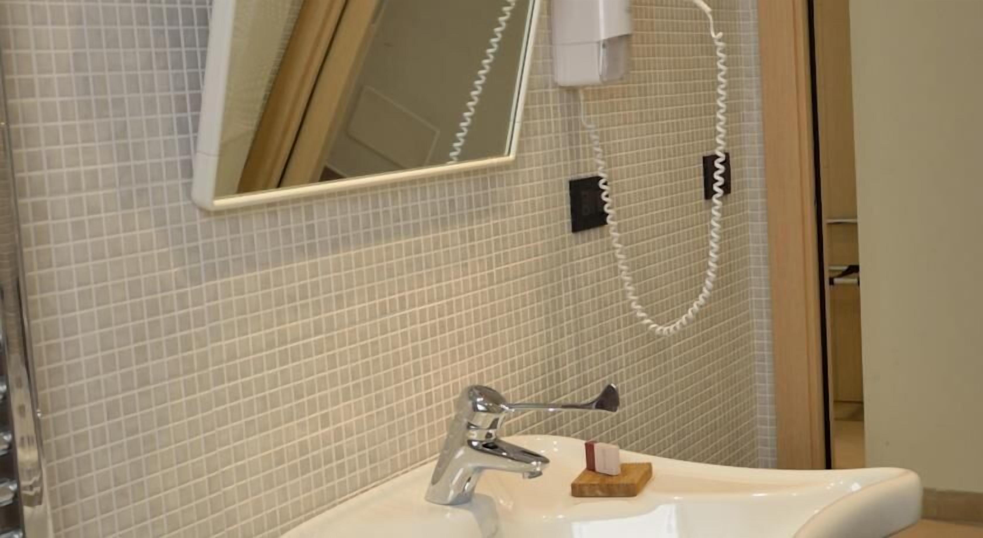 A bathroom with a sink, mirror, and a telephone mounted on the wall.