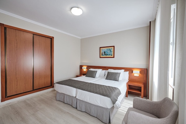 A hotel room with a large bed, a wardrobe, a nightstand, a chair, and a painting on the wall. - Hotel San Lorenzo (Santiago de Compostela)