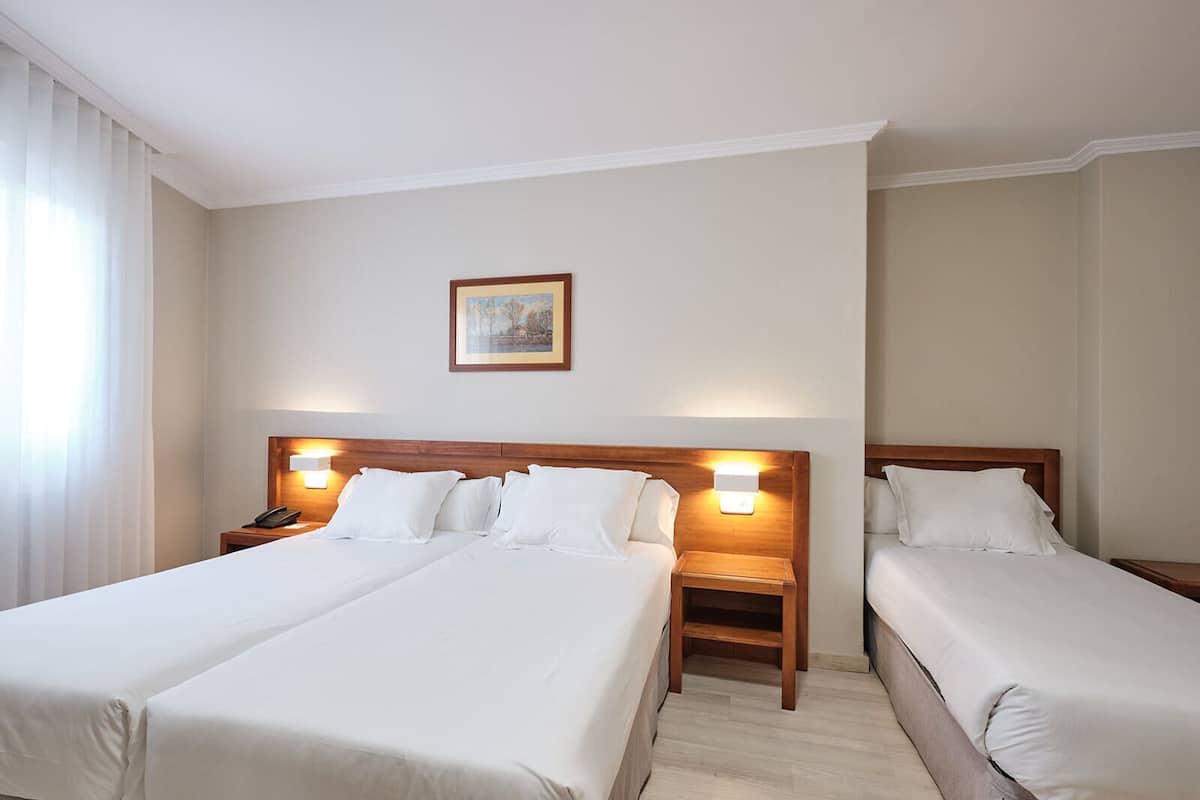 Habitación de hotel con dos camas, una mesita de noche con teléfono y un cuadro en la pared.
