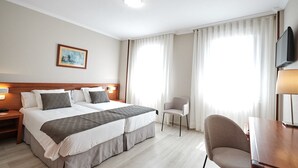 A hotel room with a double bed, a desk with a chair, a TV, and two windows with curtains. - Hotel San Lorenzo (Santiago de Compostela)