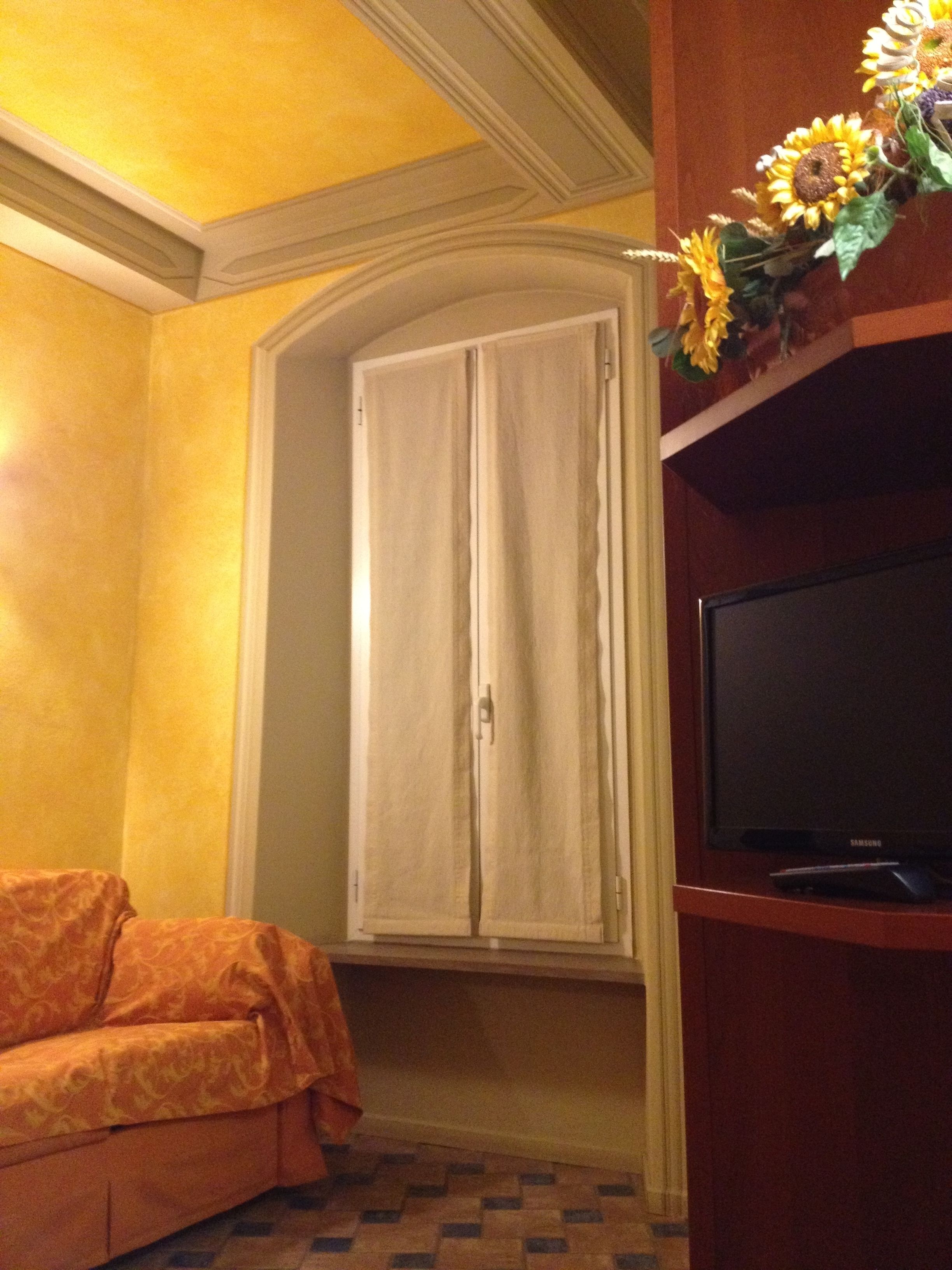 A room with a sofa, a television, and a window with curtains.