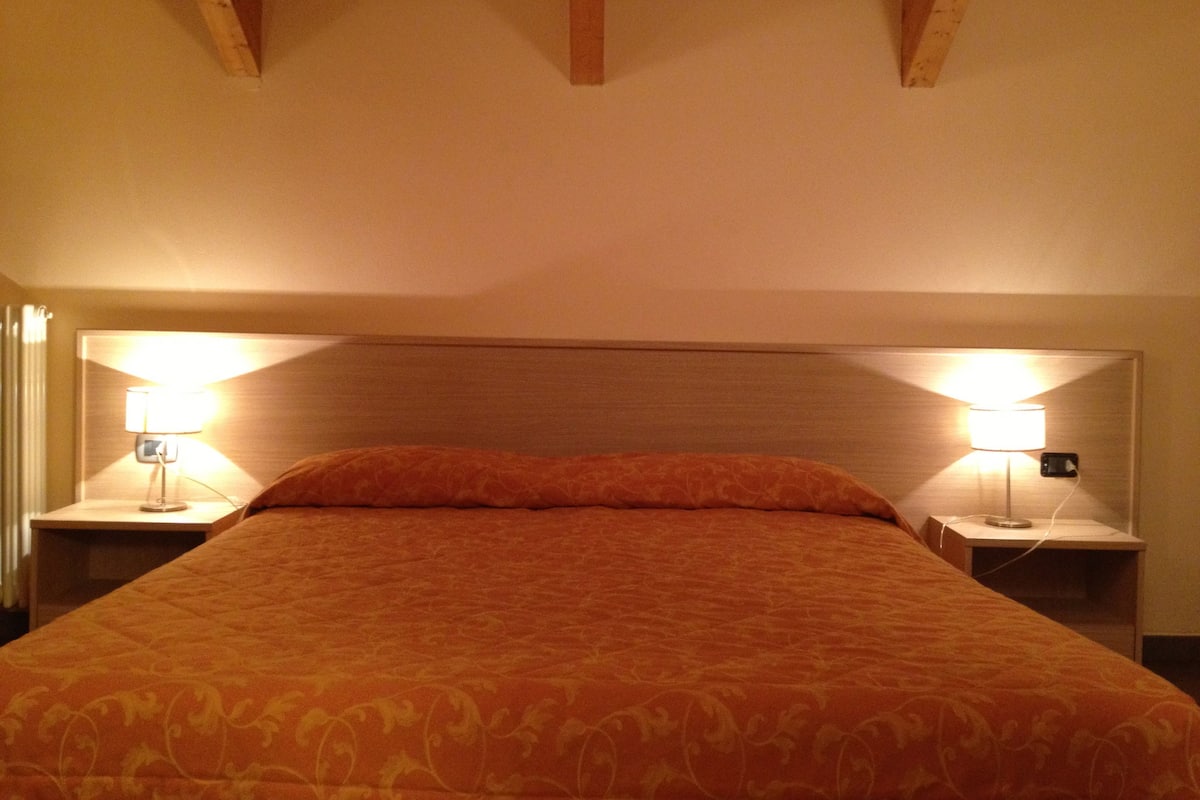 Una habitación de hotel con una cama grande, cabecero de madera y mesitas de noche con lámparas.