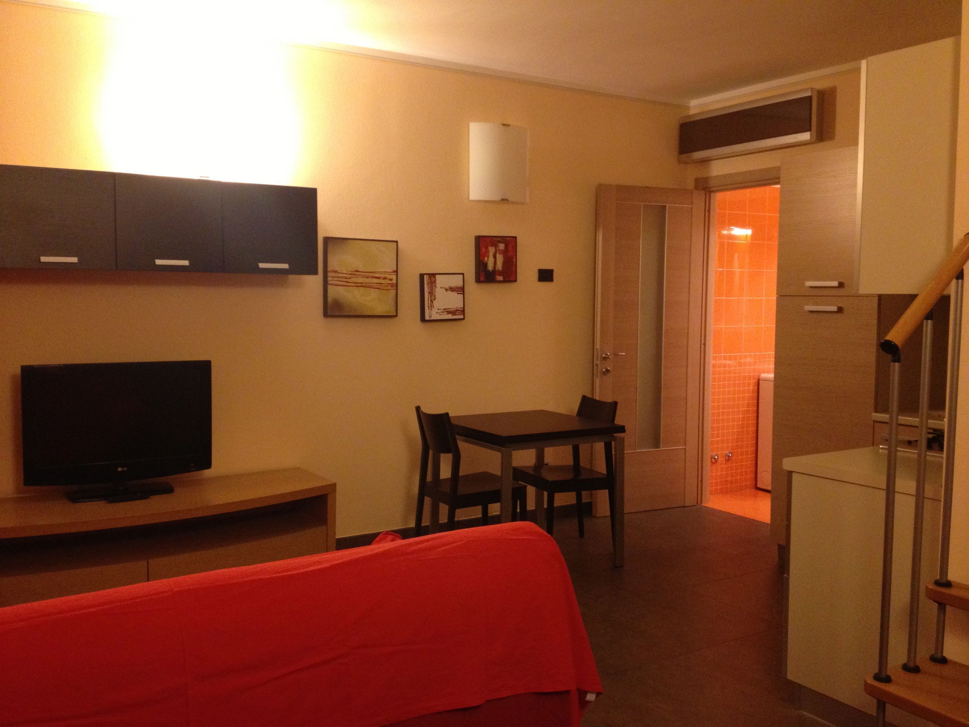 A compact living space with a TV, a dining table, and a red sofa.
