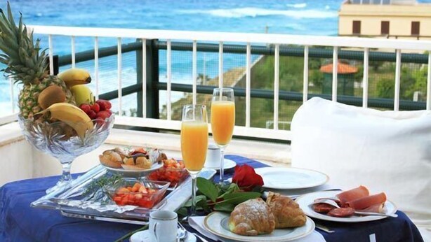 A breakfast table with fruits, pastries, and juice, overlooking a coastal view.