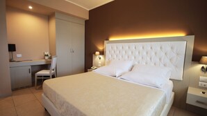 A hotel room with a bed, a desk, a chair, and a nightstand with a lamp.