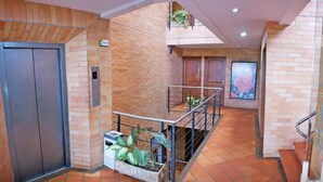 A hotel lobby with a brick wall, a metal staircase, and a tiled floor. - Hotel Torre del Prado (Barranquilla)