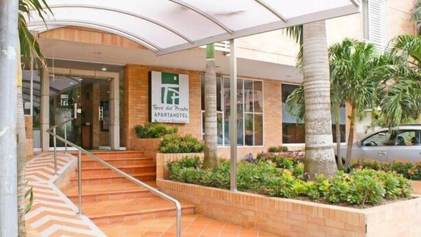 An entrance to an apartment hotel with a covered outdoor area, a staircase, and a sign indicating the name. - Hotel Torre del Prado (Barranquilla)
