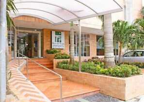 Una entrada a un hotel-apartamento con un espacio exterior cubierto, una escalera y un cartel con el nombre.