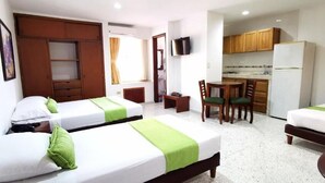 A hotel room with two single beds, a kitchenette, a dining area, and a TV mounted on the wall. - Hotel Torre del Prado (Barranquilla)